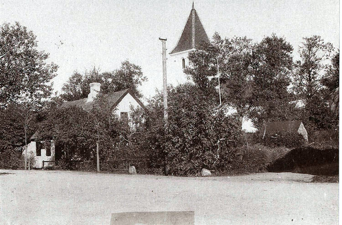 Malling Kirke med det lille, hvide hus., som hørte til kirken. Her boede skolelæreren og senere ringeren og graveren, og det er sandsynligvis Mallings første skole. Til højre ses hjørnet af Stenhøjgård, der blev flyttet til Tværgade i 1903. Det lille kampestenshus var Mallings sprøjtehus. 